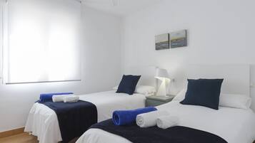 Hotellihuone, jossa on kaksi sänkyä. Kummassakin sängyssä on valkoinen ja tummansininen päiväpeite, yöpöydällä on lamppu ja seinällä on taulu.