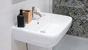 Un lavabo de salle de bain blanc, doté d’un robinet moderne, d’un distributeur de savon et d’un porte-savon en bois.