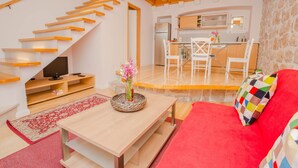 Un intérieur moderne avec un escalier en bois, un coin cuisine et un canapé rouge agrémenté d’un coussin coloré.