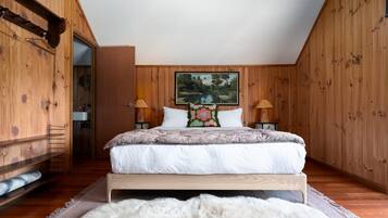 Ein Schlafzimmer mit Holzbalkendecke, einem Bett mit weißer Bettwäsche, zwei Nachttischlampen, einem Bild an der Wand und einem Fellteppich auf dem Boden.