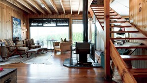 Interior acolhedor de uma cabana, com piso de madeira, lareira e escada.