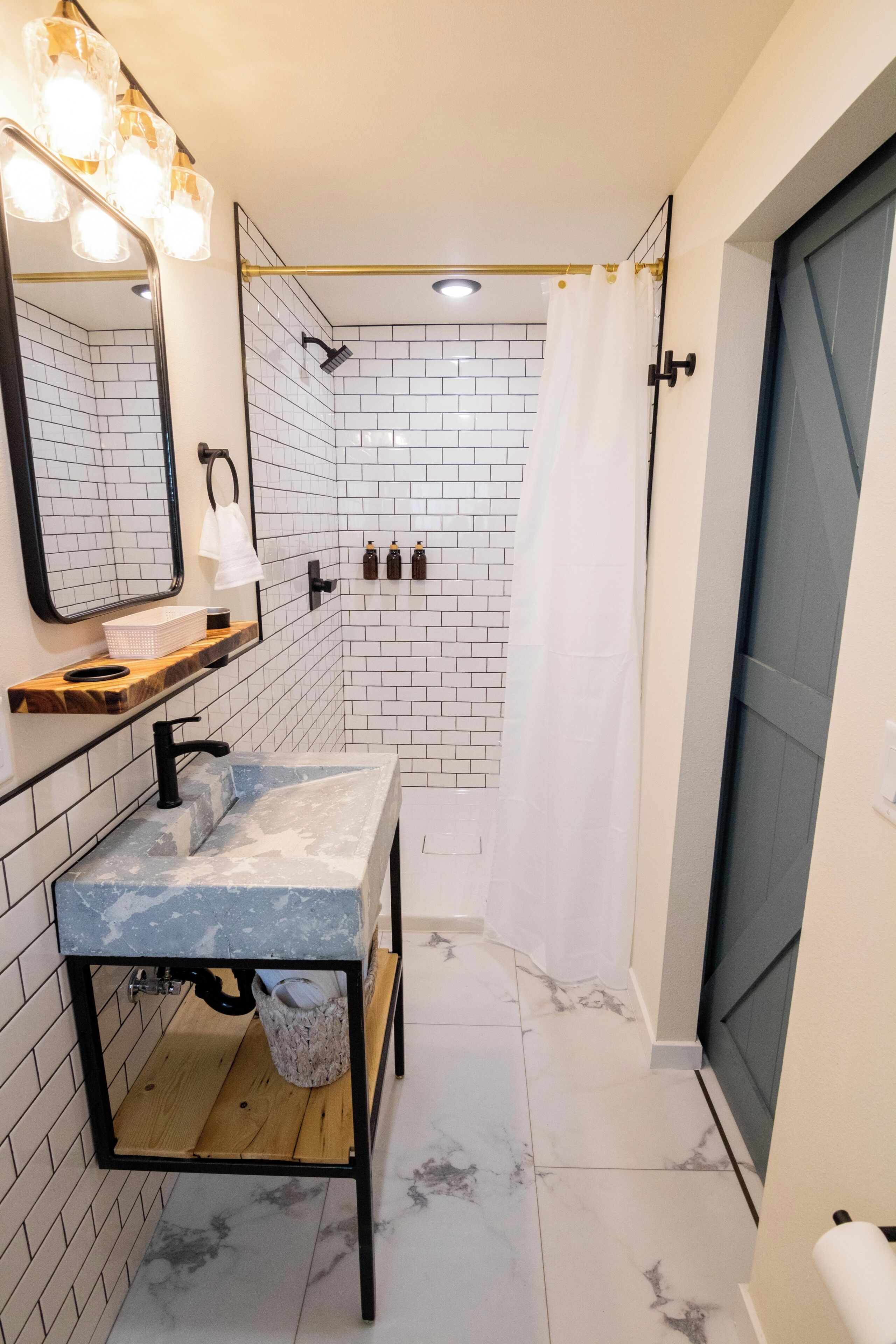 A bathroom with a marble sink, a mirror with lights, a shower with a curtain, and a towel rack.