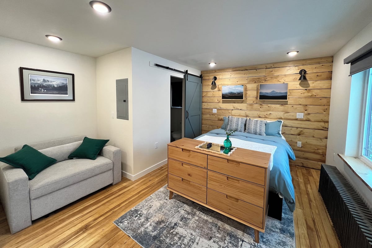 A bedroom with a bed, a dresser, a sofa, and a window.