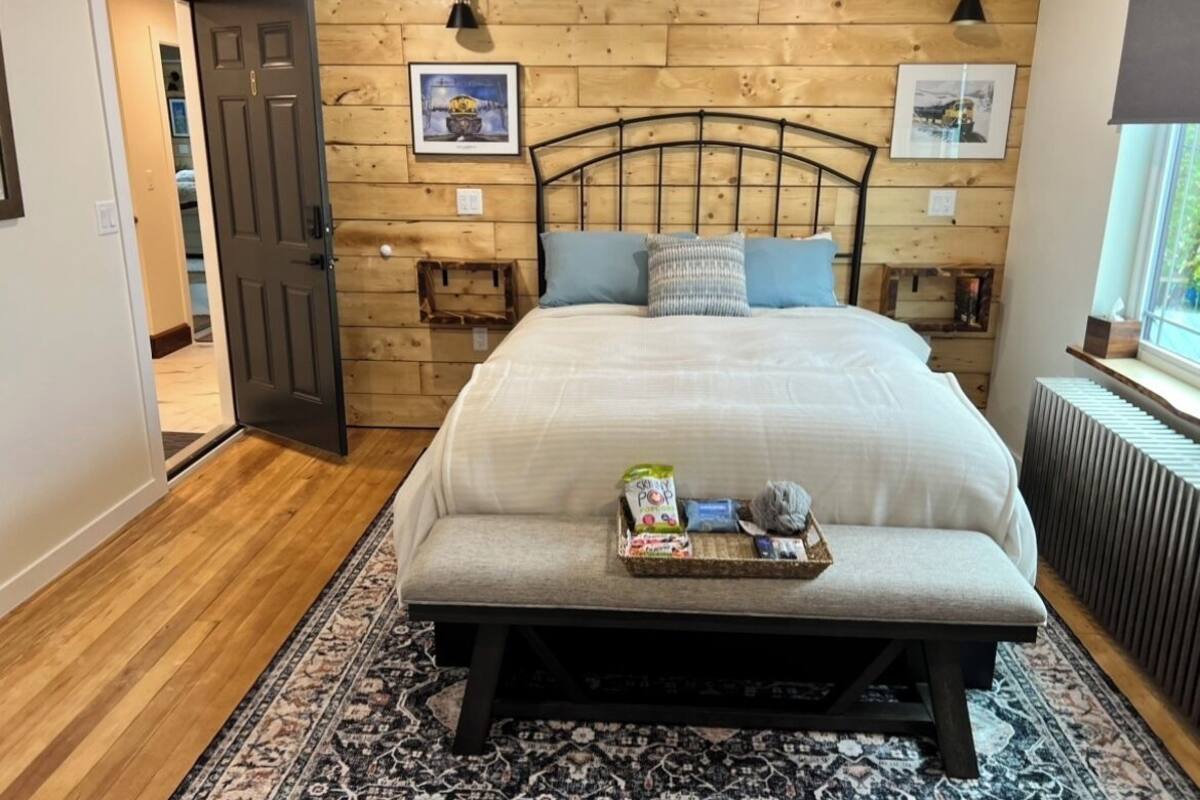 A bedroom with a wooden headboard, a bed with pillows, a bedside table with a tray of items, and a window with a view.