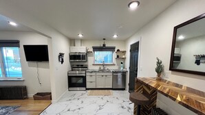 A modern kitchen with stainless steel appliances, a marble floor, and a wooden bar area. - Dollhouse Downtown (Fairbanks)