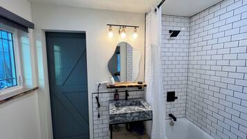 A bathroom with a shower, a sink with a mirror, and a window.