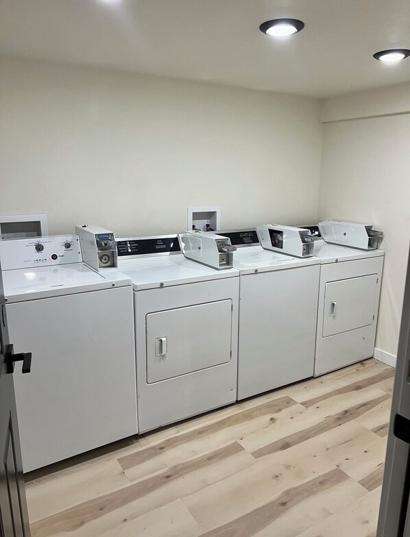 A laundry facility with four washing machines and a dryer, arranged in a row. - Dollhouse Downtown (Fairbanks)