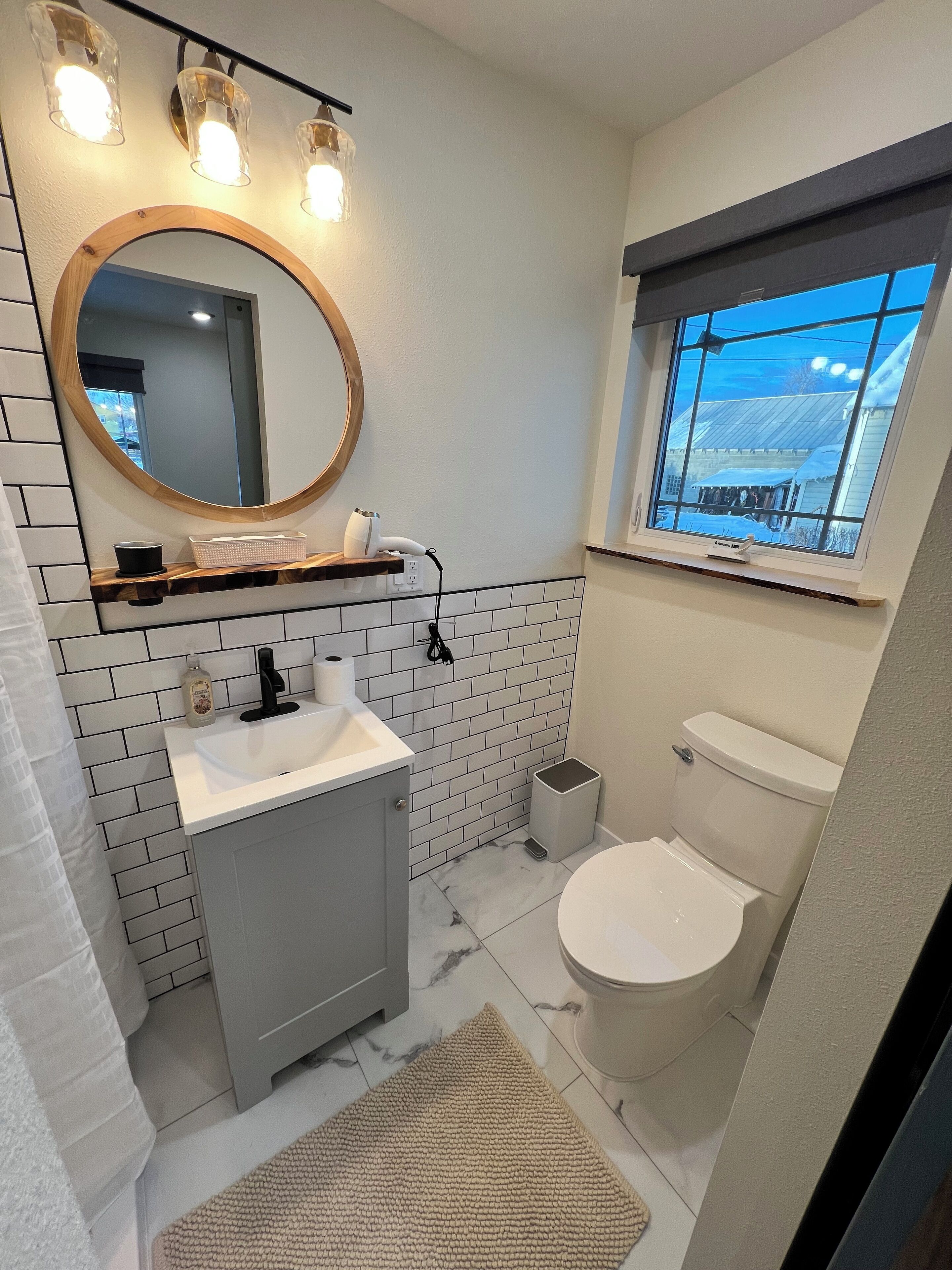 A modern bathroom with a white sink, mirror, and toilet. There is a window with a view of a snowy landscape.