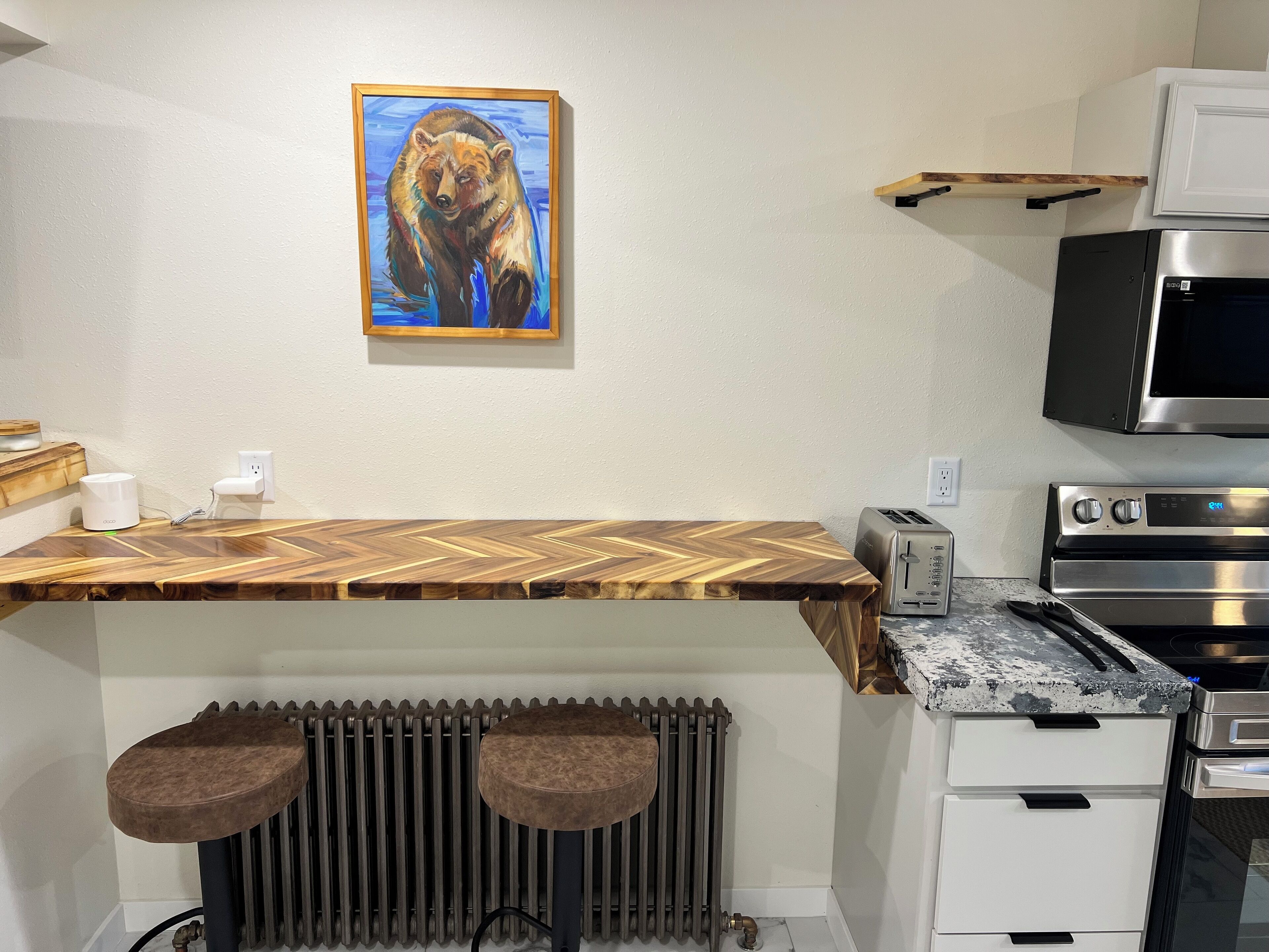 A kitchen with a wooden countertop, a toaster, a microwave, and a stove. There is a radiator below the countertop and a framed picture on the wall.
