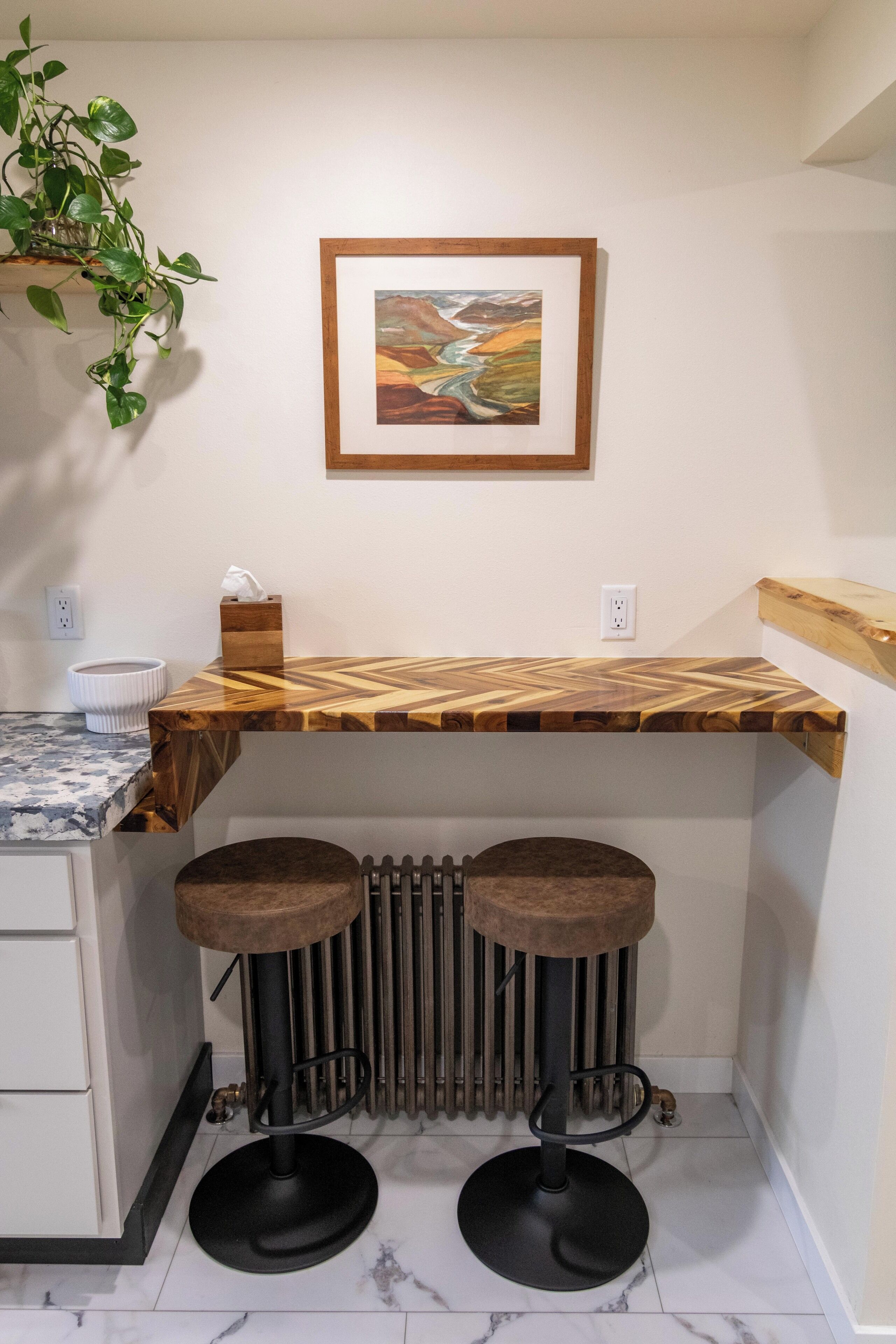 Een keuken met een houten aanrecht, twee barkrukken, een radiator en een lijst met een schilderij aan de muur.
