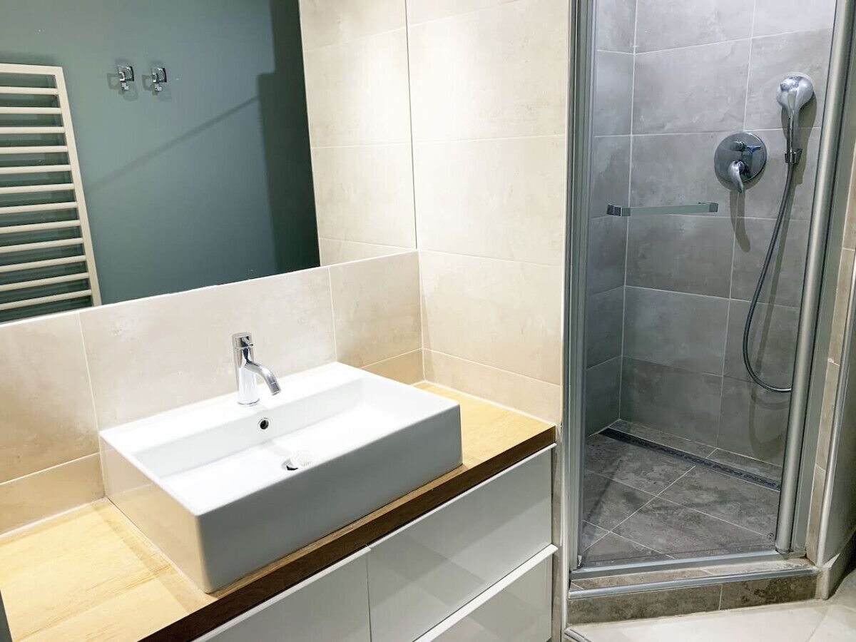 A bathroom with a white sink, a shower, and a mirror.