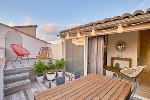 A rooftop terrace with a wooden table and chairs, potted plants, and a sliding glass door leading to an interior space. - Calm and bright; Terrace and panoramic view in the center<br>Housing (Arles)