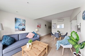Una sala de estar moderna con un sofá gris, una mesa de centro de madera y un comedor con una mesa redonda y sillas.
