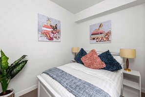 A bedroom with a bed, two nightstands, a lamp, a potted plant, and two wall-mounted artworks. - A Cozy & Comfy 2BR Apt Near Victoria Market (Melbourne)