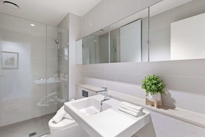 A modern bathroom with a glass shower enclosure, a white sink, and a large mirror above the vanity.