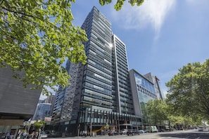 A modern high-rise building with a glass facade, surrounded by trees and other buildings.