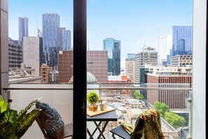 A balcony with a city view, a small table with a plant, and a chair. - A Cozy & Comfy 2BR Apt Near Victoria Market (Melbourne)