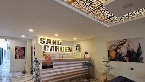 A reception area with a marble floor, a reception desk, a black sofa, and decorative ceiling panels. - SAND GARDEN (Bodrum)
