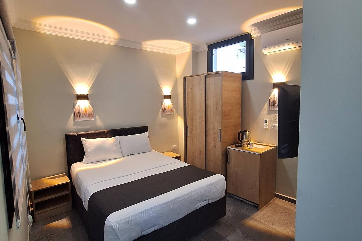 Une chambre d’hôtel moderne dotée d’un grand lit, de lampes de chevet, d’une armoire, d’un petit bureau avec une lampe et d’un téléviseur fixé au mur.