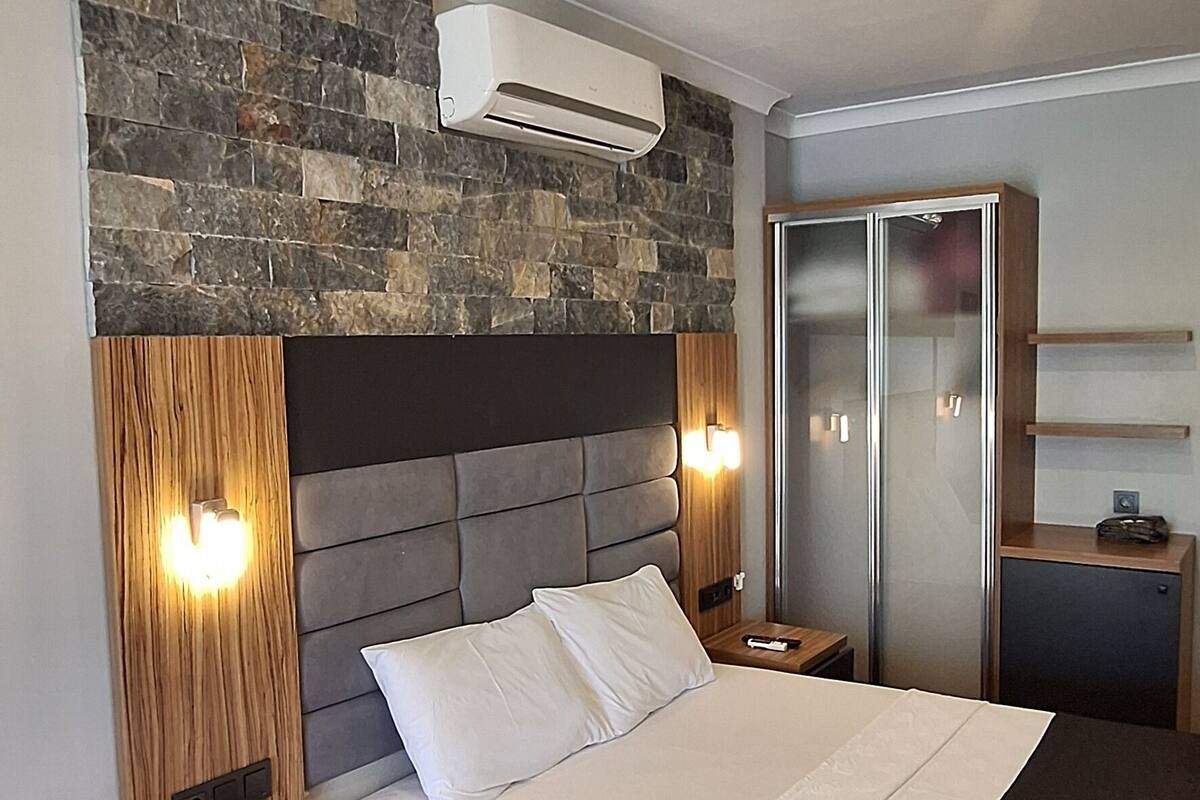 Une chambre moderne avec un mur d’accent en pierre, un grand lit avec du linge de lit blanc, des tables de chevet en bois et une armoire intégrée avec un miroir.