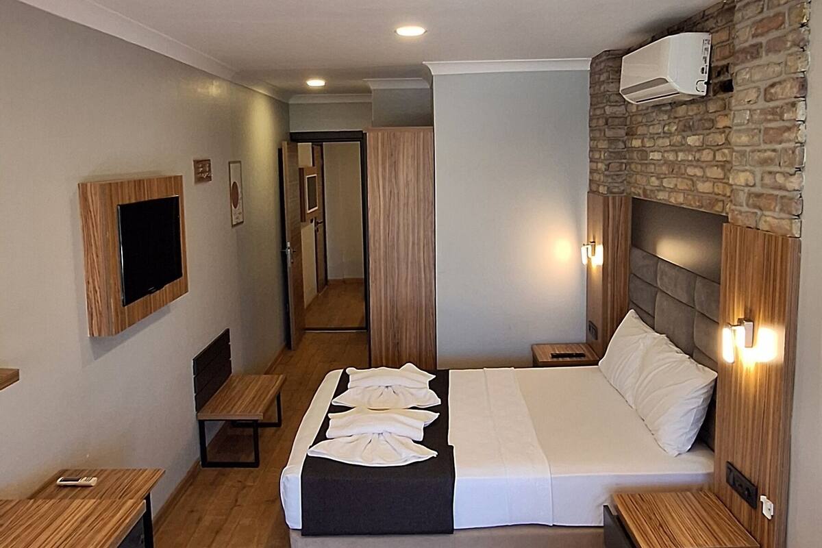 Une chambre d’hôtel moderne dotée d’un grand lit, d’un plancher en bois, d’un téléviseur fixé au mur et d’une cheminée en pierre.