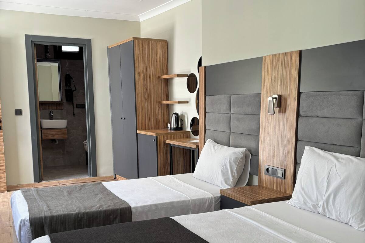 Une chambre d’hôtel avec deux lits, une armoire en bois, une petite étagère avec des articles de toilette et un miroir.