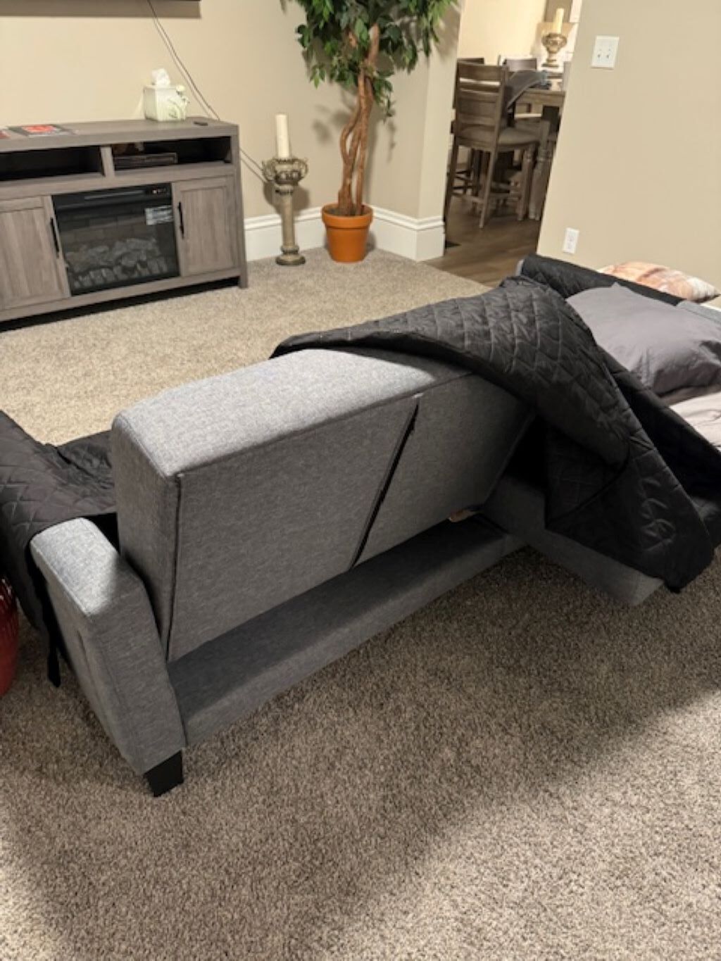 A grey sofa with a black throw blanket, a potted plant, and a dining area in the background.