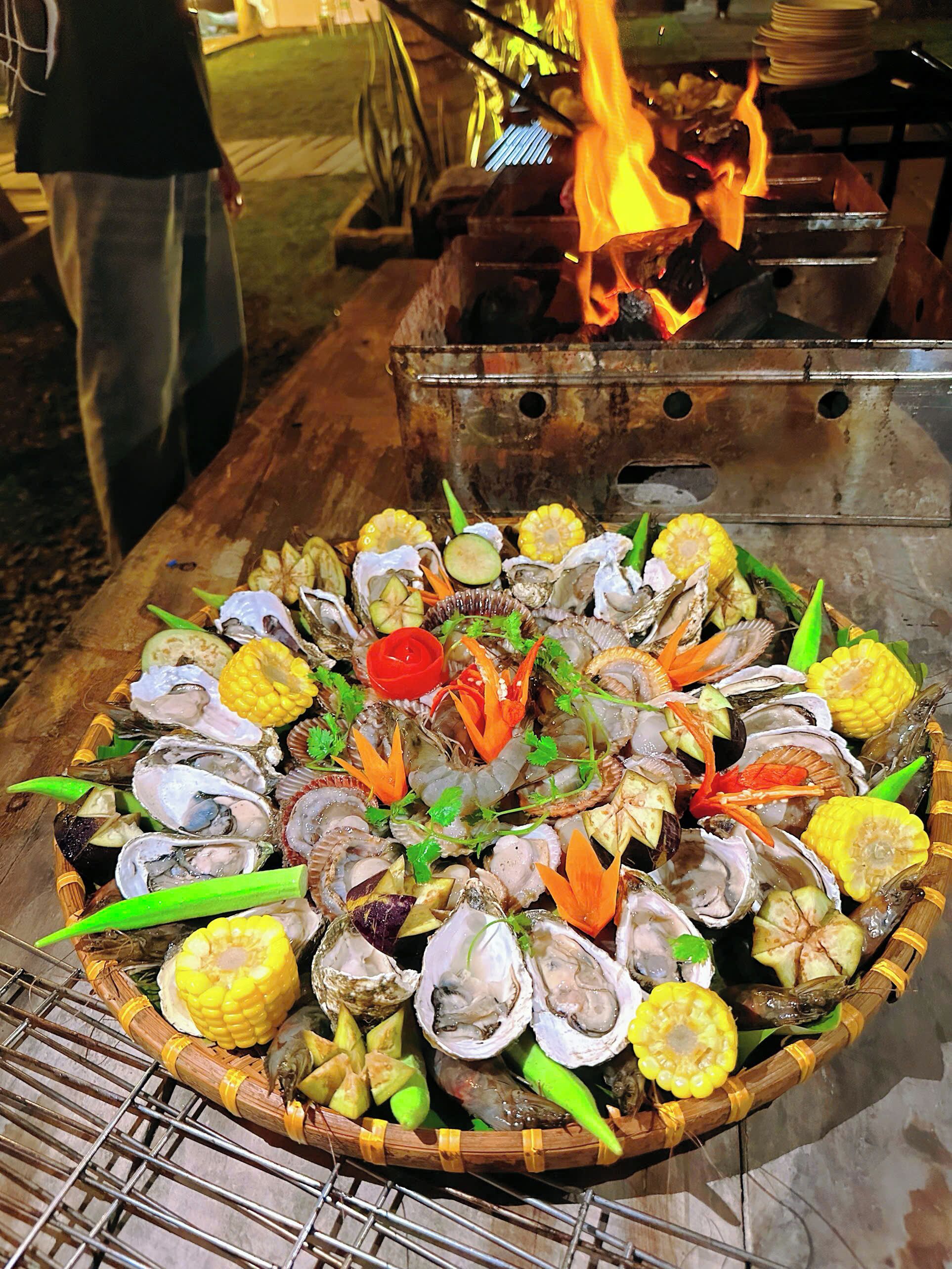 A large, round, woven basket filled with various seafood items, including oysters, shrimp, and corn, displayed on a metal rack.