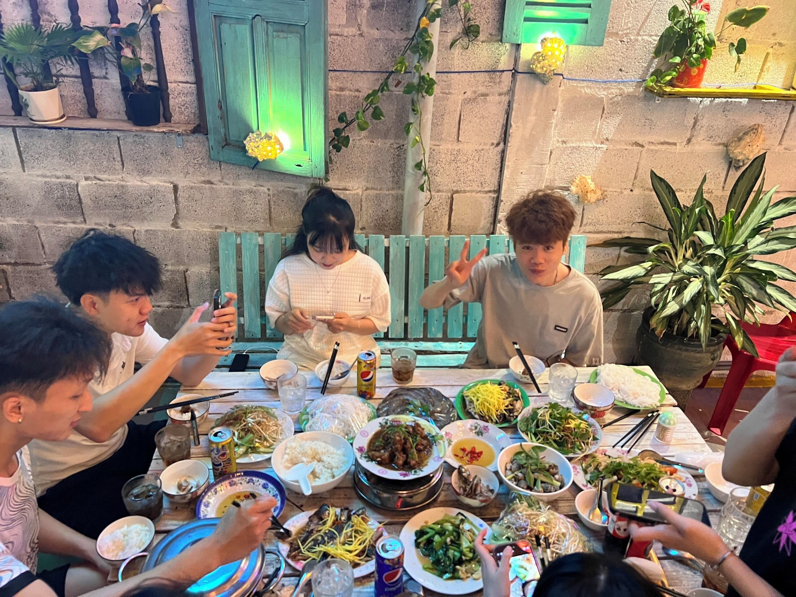 Un groupe de personnes est réuni autour d’une table, où se trouvent divers plats et boissons.