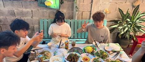 Un groupe de personnes est réuni autour d’une table, où se trouvent divers plats et boissons.