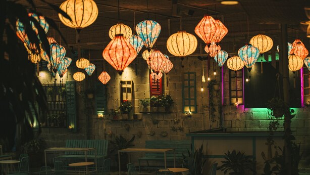 A dimly lit restaurant with hanging paper lanterns, wooden tables, and chairs. - Dai Duong Lagi Homestay & Coffee (Phuoc Hoi)