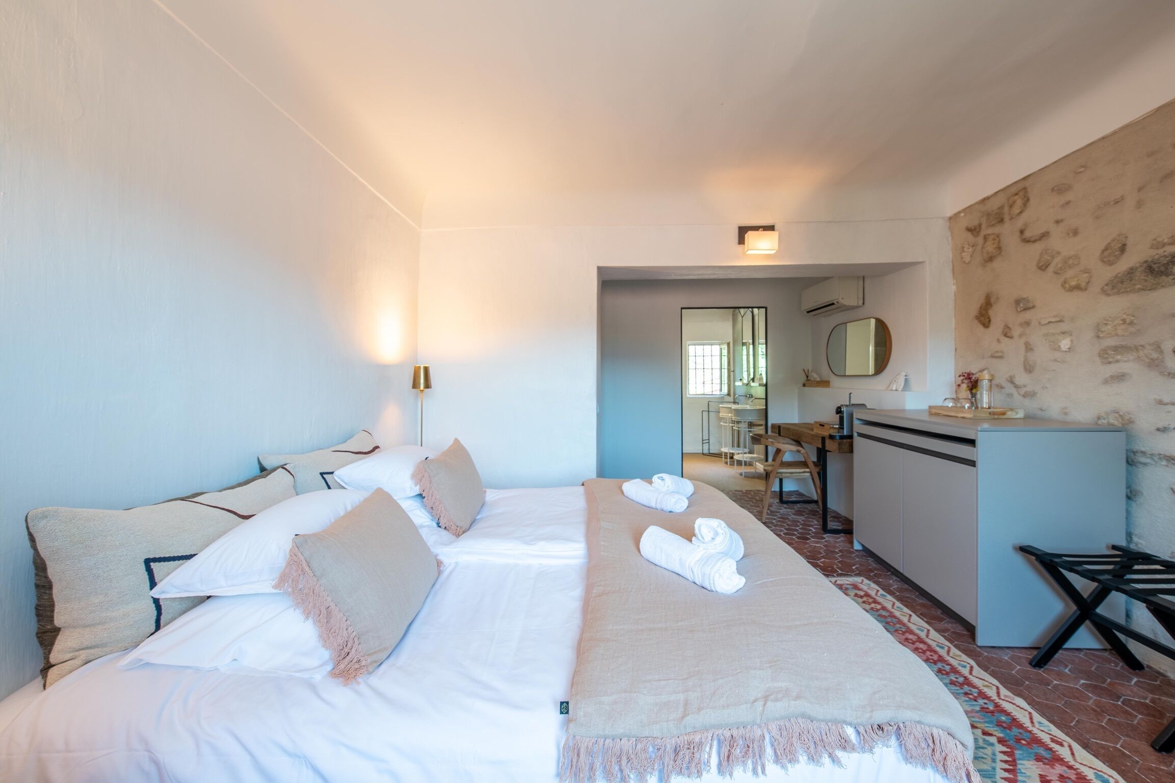 Una habitación de hotel con cama, escritorio y baño visible a través de una puerta abierta.