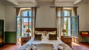 A spacious bedroom with a large bed, two bedside tables, and a view through open windows.