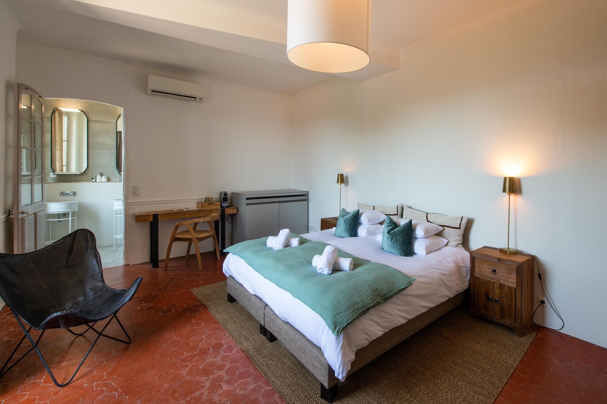 Una habitación de hotel con cama, escritorio, silla, mesita de noche y lámpara.