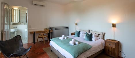 A hotel room with a bed, a desk, a chair, a nightstand, and a lamp.