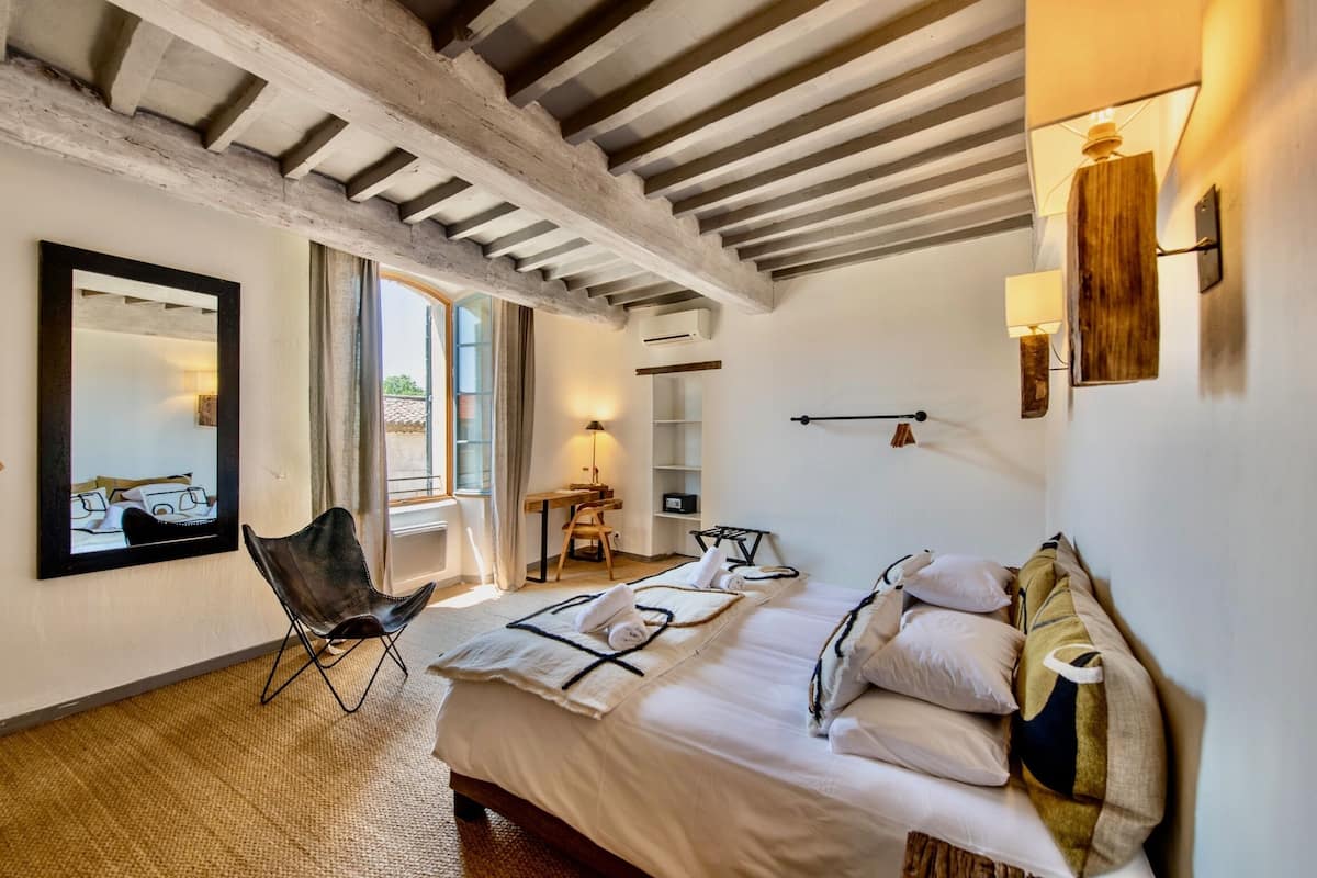 A bedroom with a large bed, a chair, a desk, and a mirror.