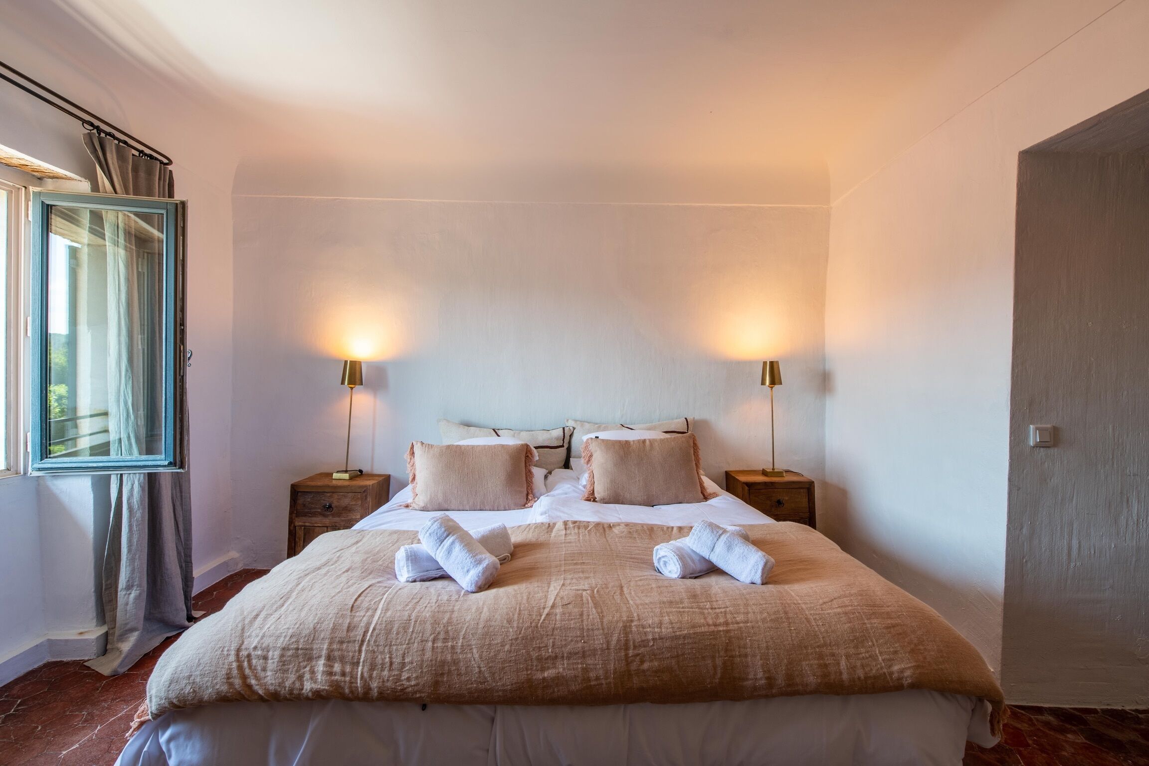 A hotel room with a large bed, two bedside tables, and a window with curtains.