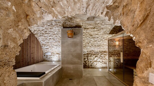 A spa room with a stone wall, a wooden slat wall, a bathtub, and a glass shower enclosure.
