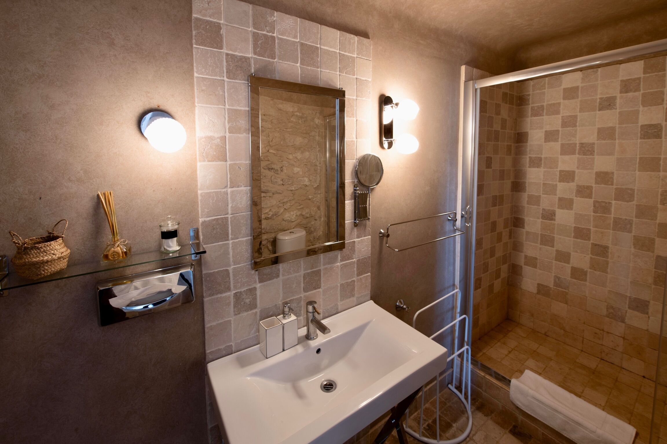 A bathroom with a glass shelf, a sink, a mirror, and a shower area.