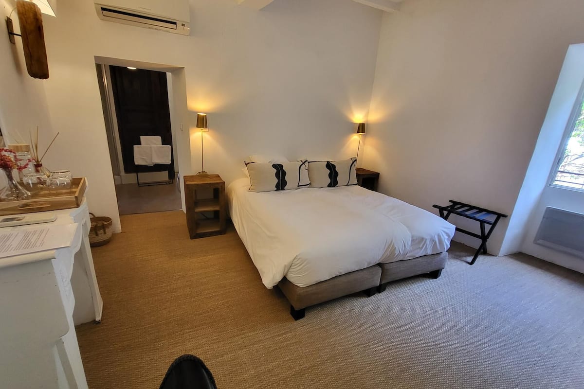 A bedroom with a bed, bedside lamps, a small table, and a window.