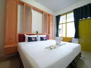 A hotel room with a large bed, a headboard with vertical panels, a window with curtains, and a yellow door. - RoomQuest Hotel Pratunam (Bangkok)