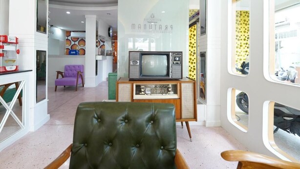 A living room with a green leather armchair, a vintage television set on a wooden cabinet, and a purple armchair. - RoomQuest Hotel Pratunam (Bangkok)