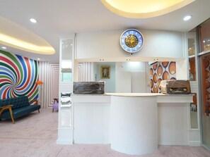 A reception area with a modern design, featuring a central clock, a counter, and a colorful wall with a spiral pattern. - RoomQuest Hotel Pratunam (Bangkok)