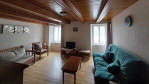 Een gezellige woonkamer met een houten plafond, een groene bank, een houten salontafel, een televisie en een schilderij aan de muur.