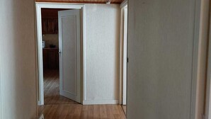 Een gang met houten vloer en een witte deur die uitkomt in een keuken.