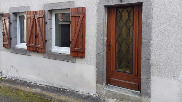 Een gebouw met een stenen gevel, een houten deur met een ruit en luiken voor de ramen.