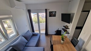 A modern living room with a grey sofa, a wooden dining table, and a potted plant. - Apartment Antonio with balcony, near the beach (Kaštel Novi)