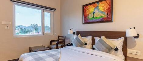 A hotel room with a bed, a chair, a desk, a window with a view, and a painting on the wall.