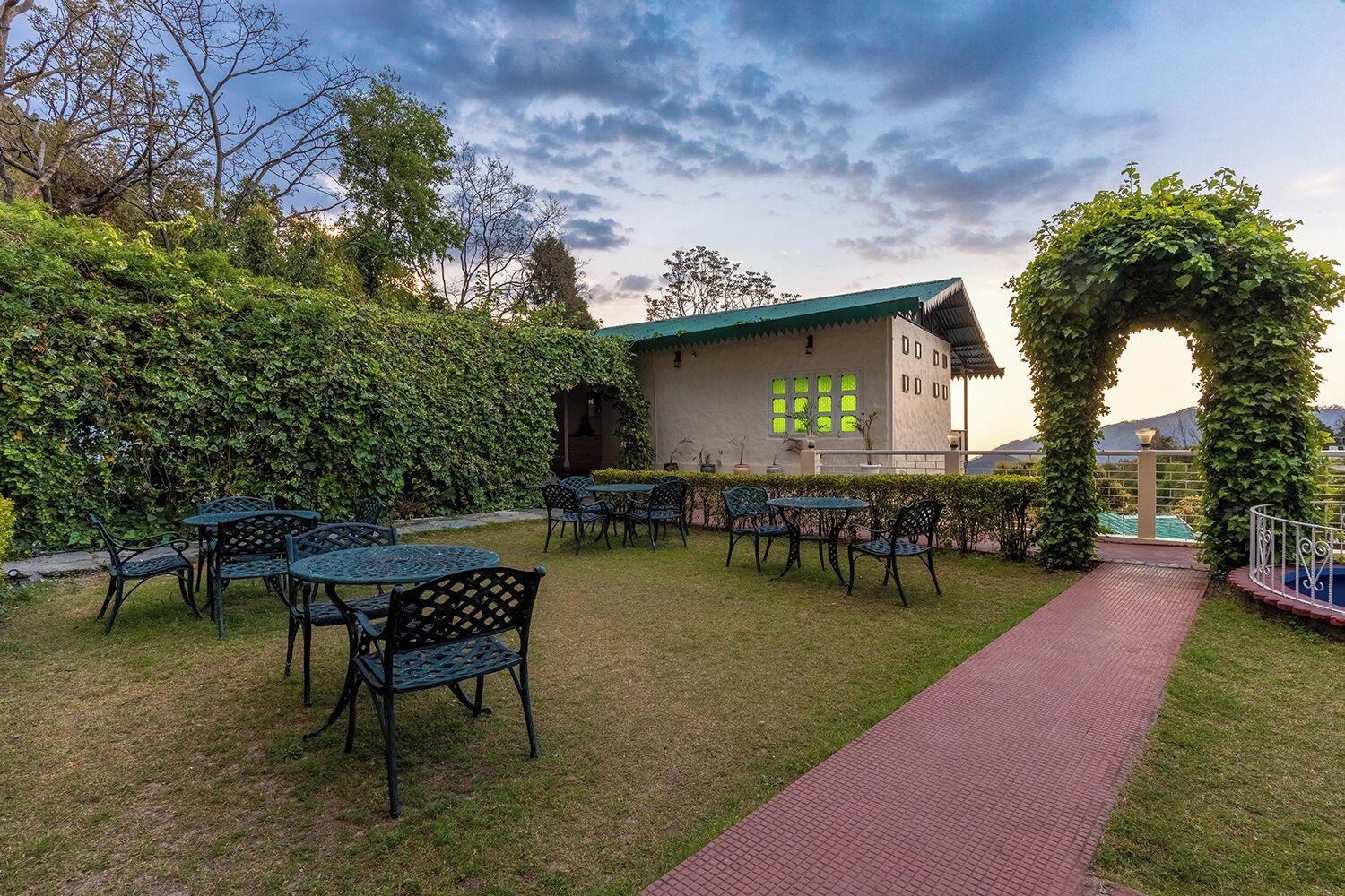An outdoor seating area with tables and chairs, a pathway, and a building with a green roof.