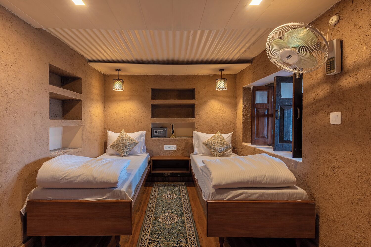 A room with two wooden beds, a small table, a radio, and a fan.